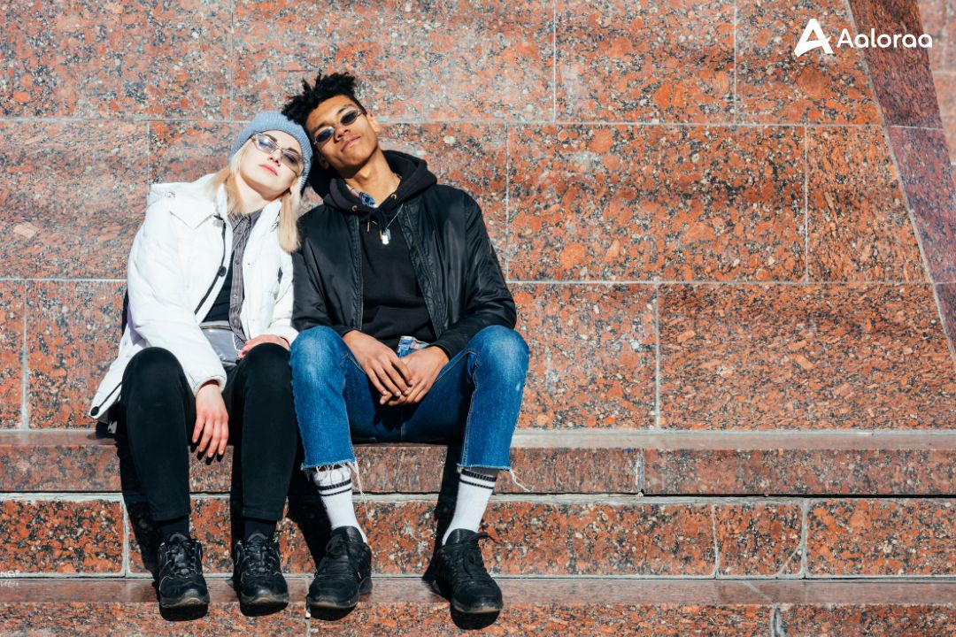 A stylish young couple sitting together on outdoor stone steps, leaning against each other under bright sunlight